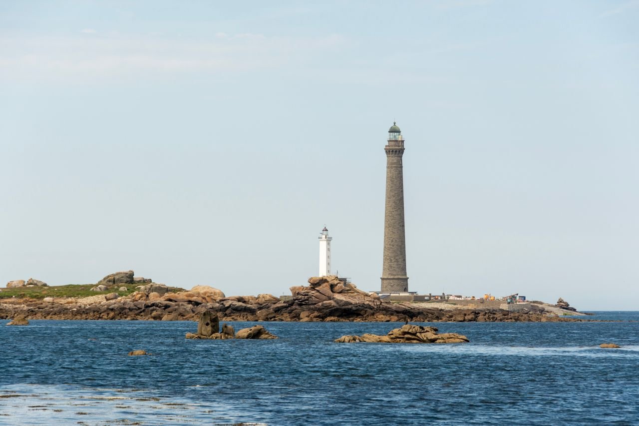 Two lighthouses stand tall on rocky shores by the sea under a clear sky.